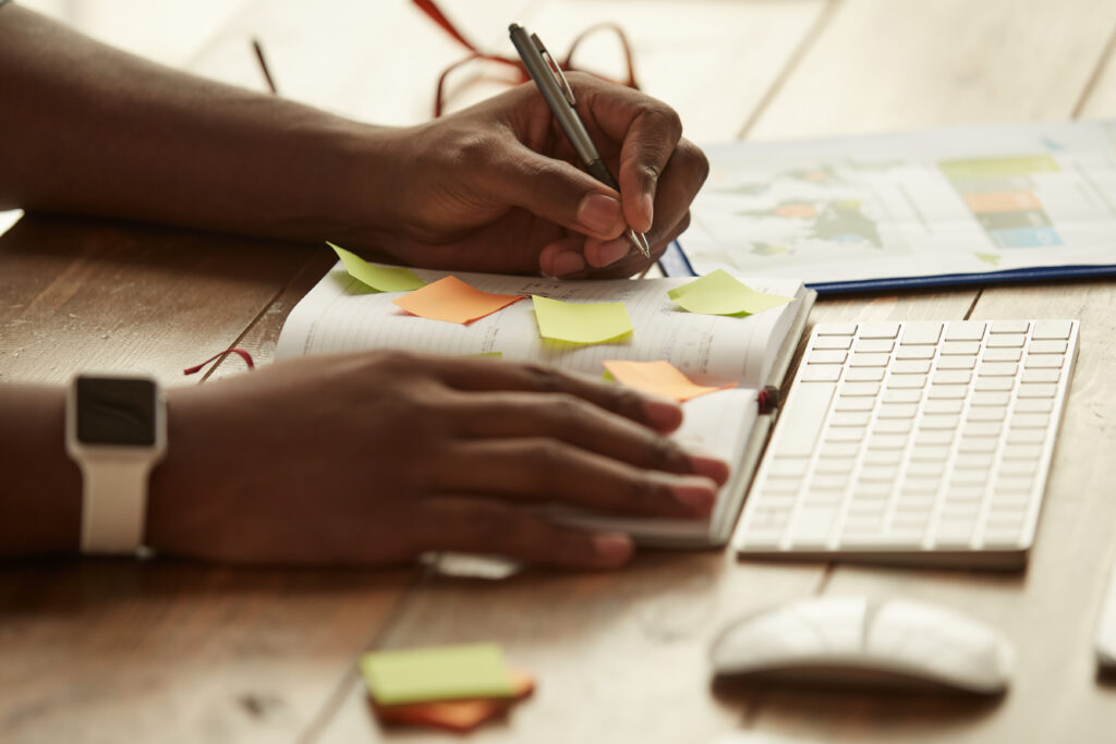 Cropped photo of afro american businessman making some notes while working remotely at home. Male hands taking notes. Freelance. Home office workplace. Correcting content strategy mistakes